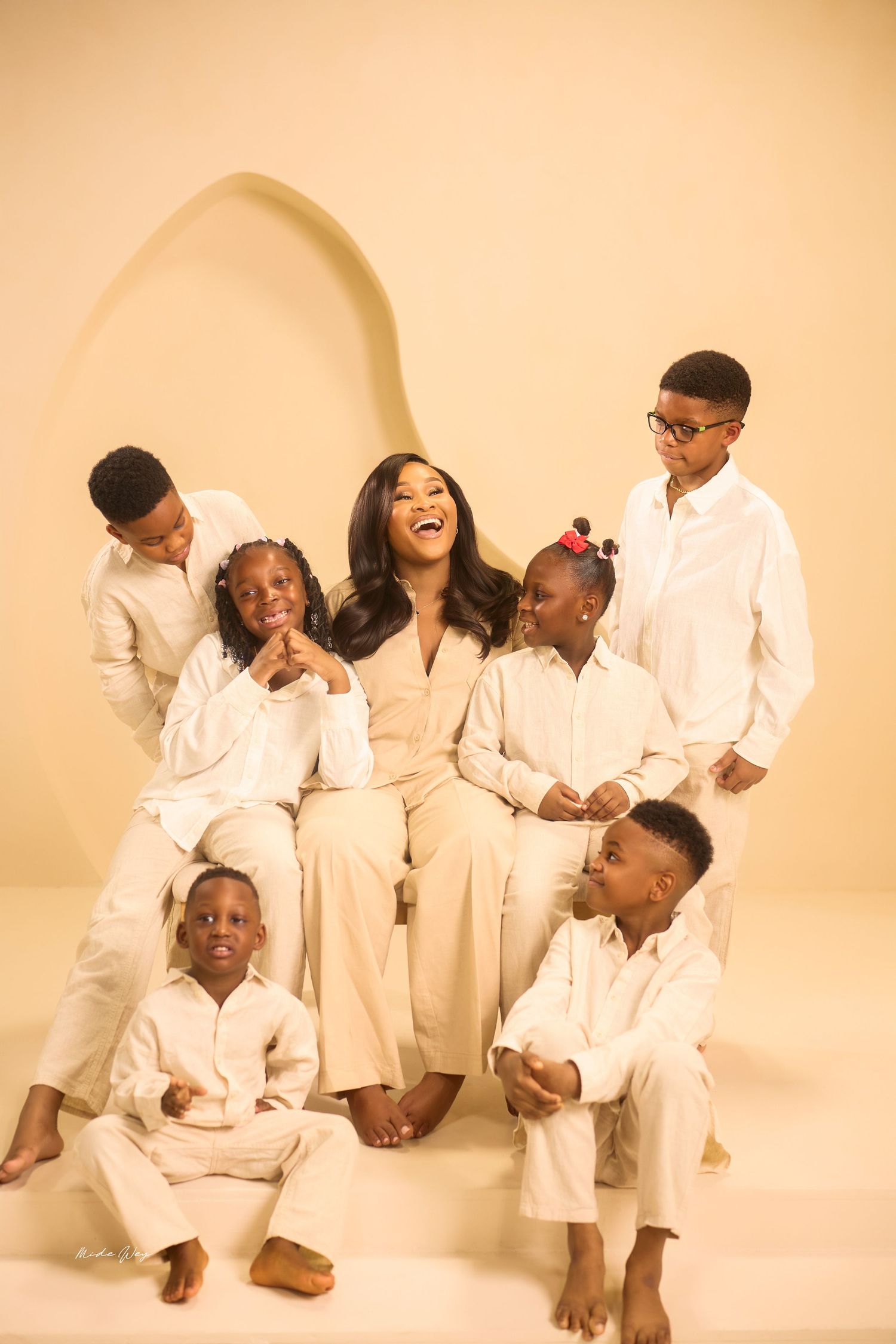 A group of people wearing all white outfits laugh and interact playfully in a bright studio setting.