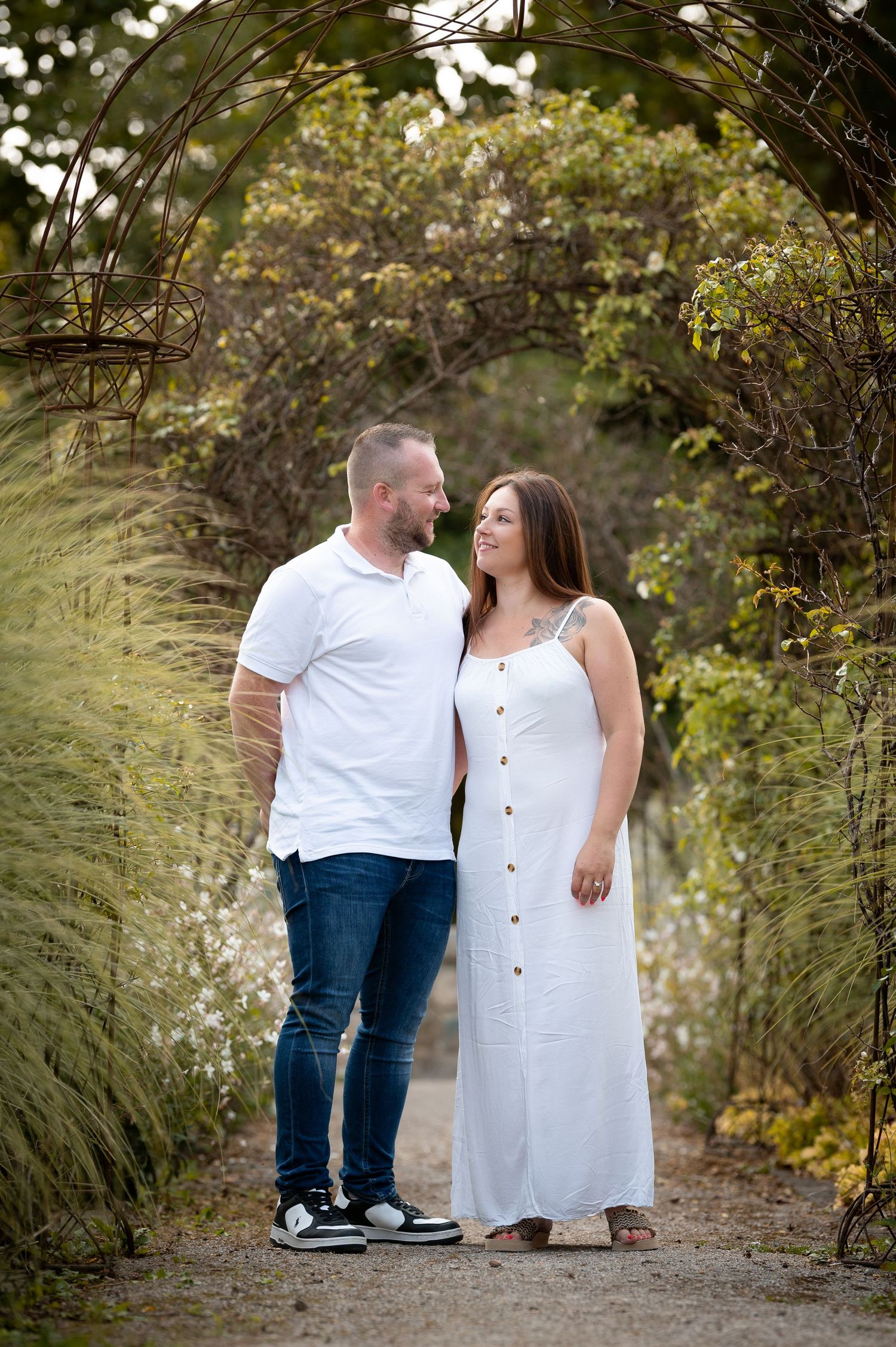 Smiling couple standing together under a rustic vine archway surrounded by natural greenery outdoors.