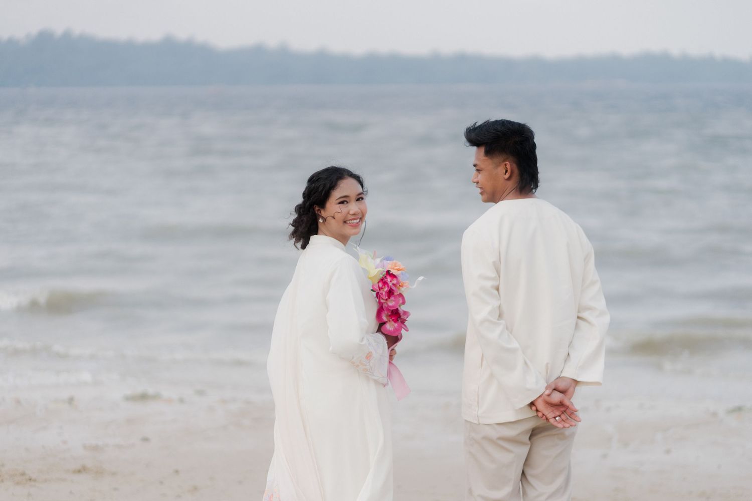 A couple in matching white outfits sits together on steps sharing an intimate moment.