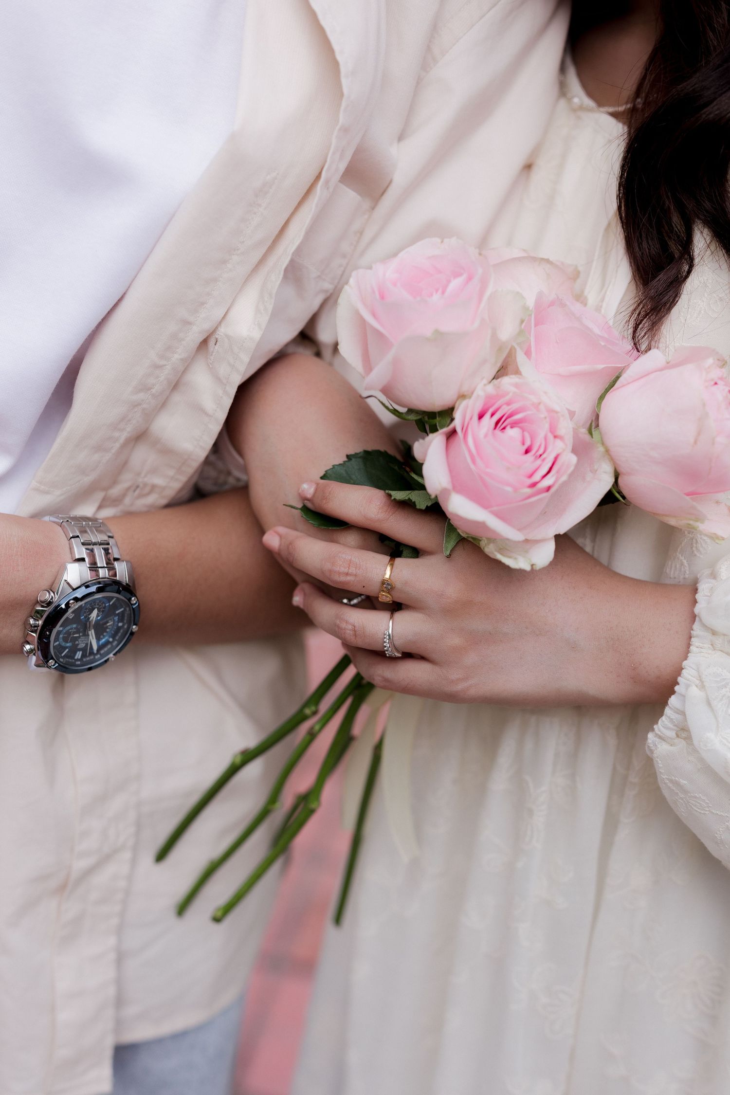 A close-up of hands showing off engagement rings against a white shirt.