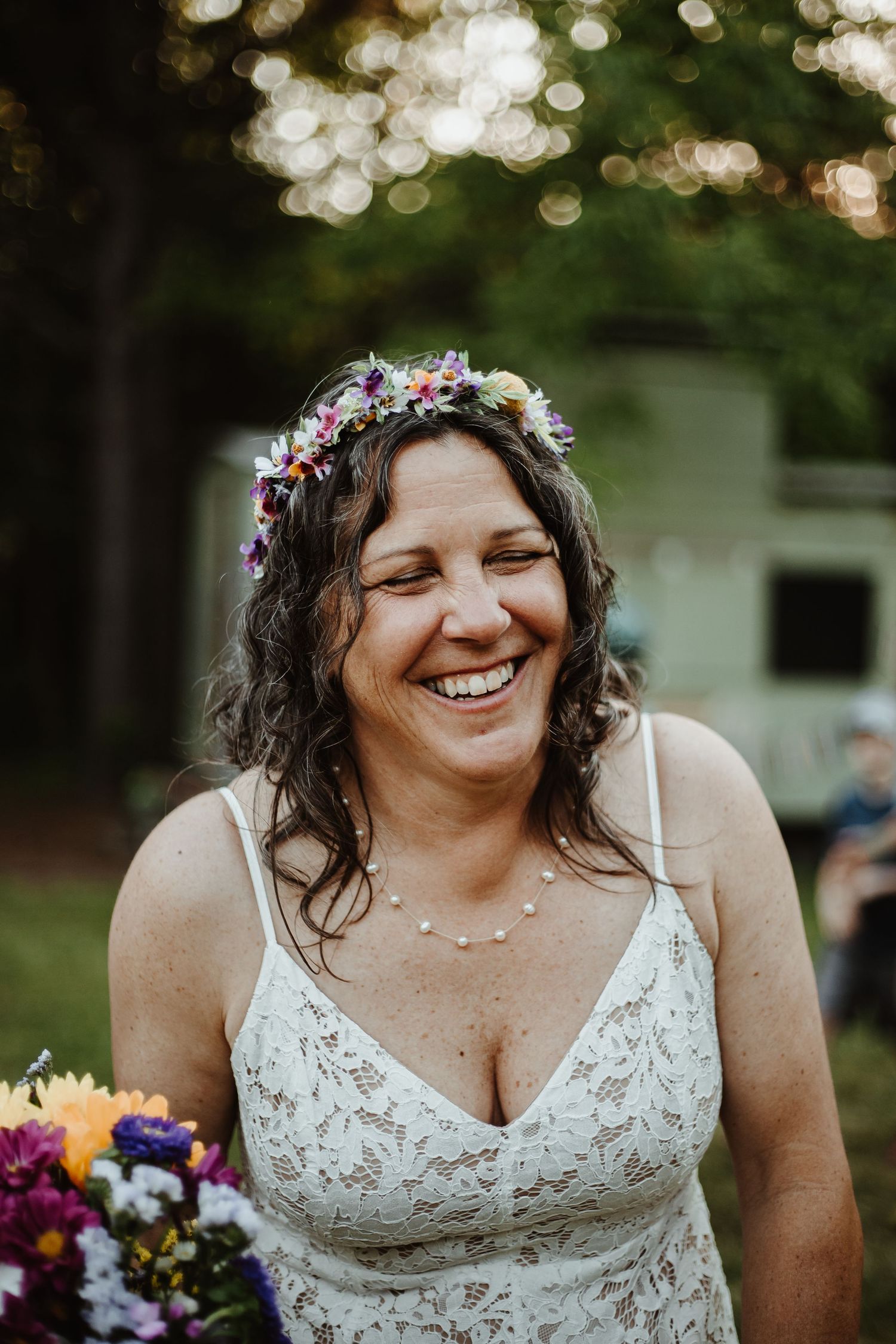 A joyful bride wearing a floral crown and lace dress holds a colorful bouquet.