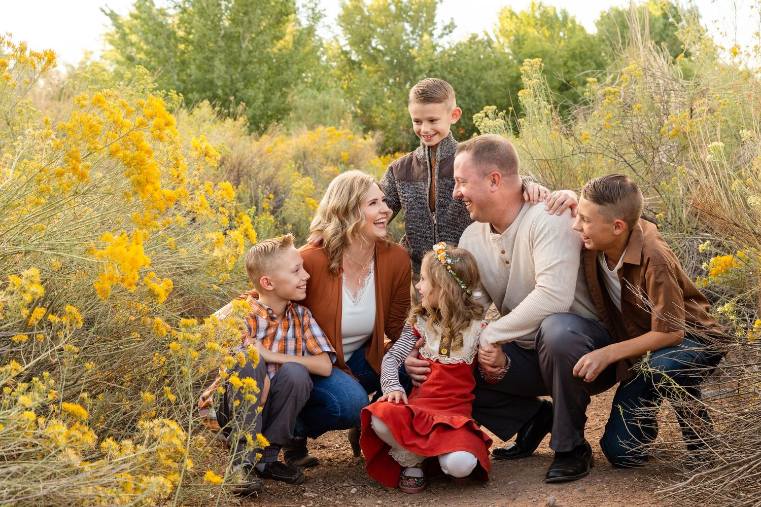 a family of 6 kneeling in a beautiful bush of yellow flowers smiling and laughing at each other