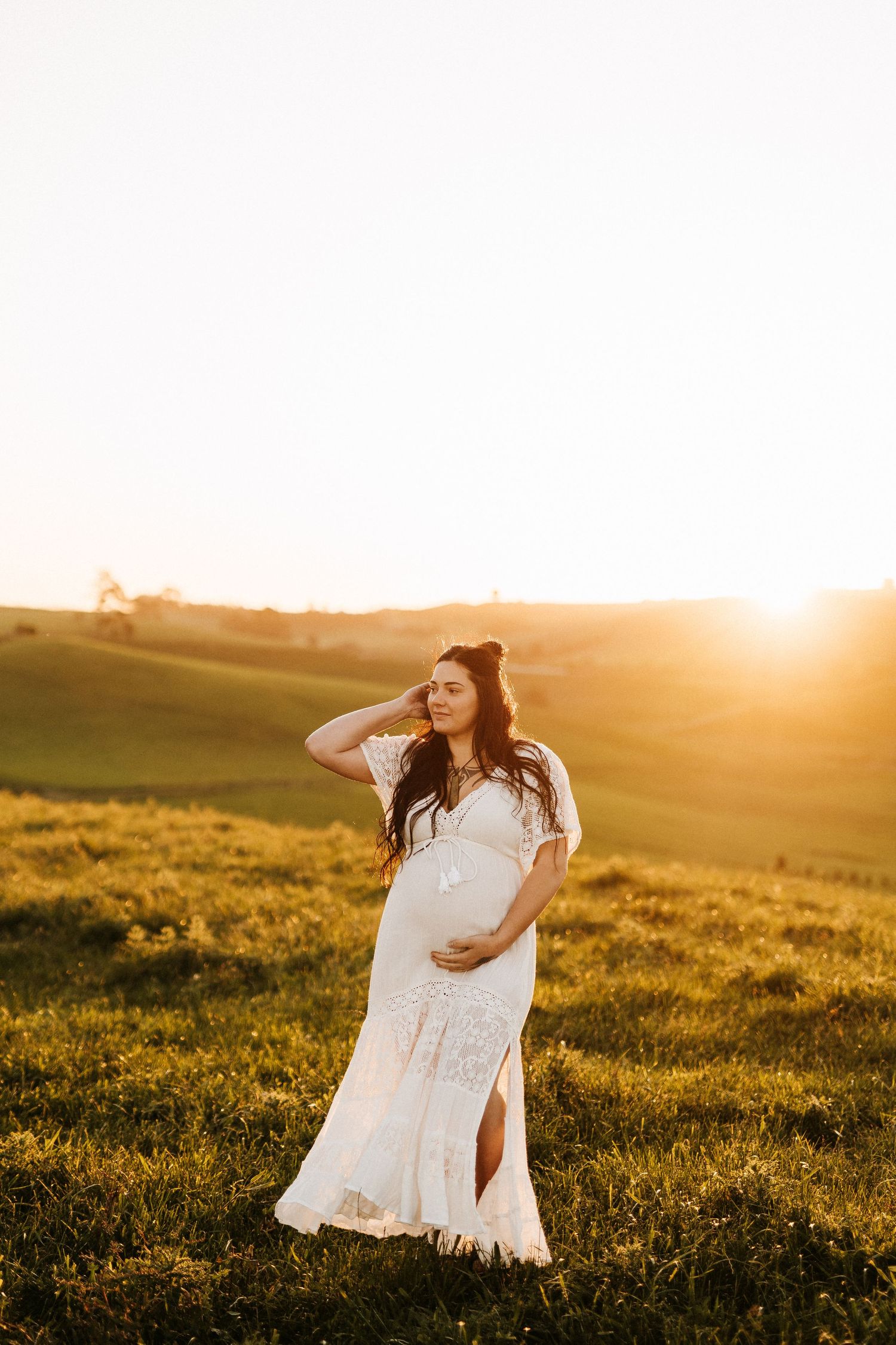 A person in a white lace dress poses in a sunlit meadow at golden hour.