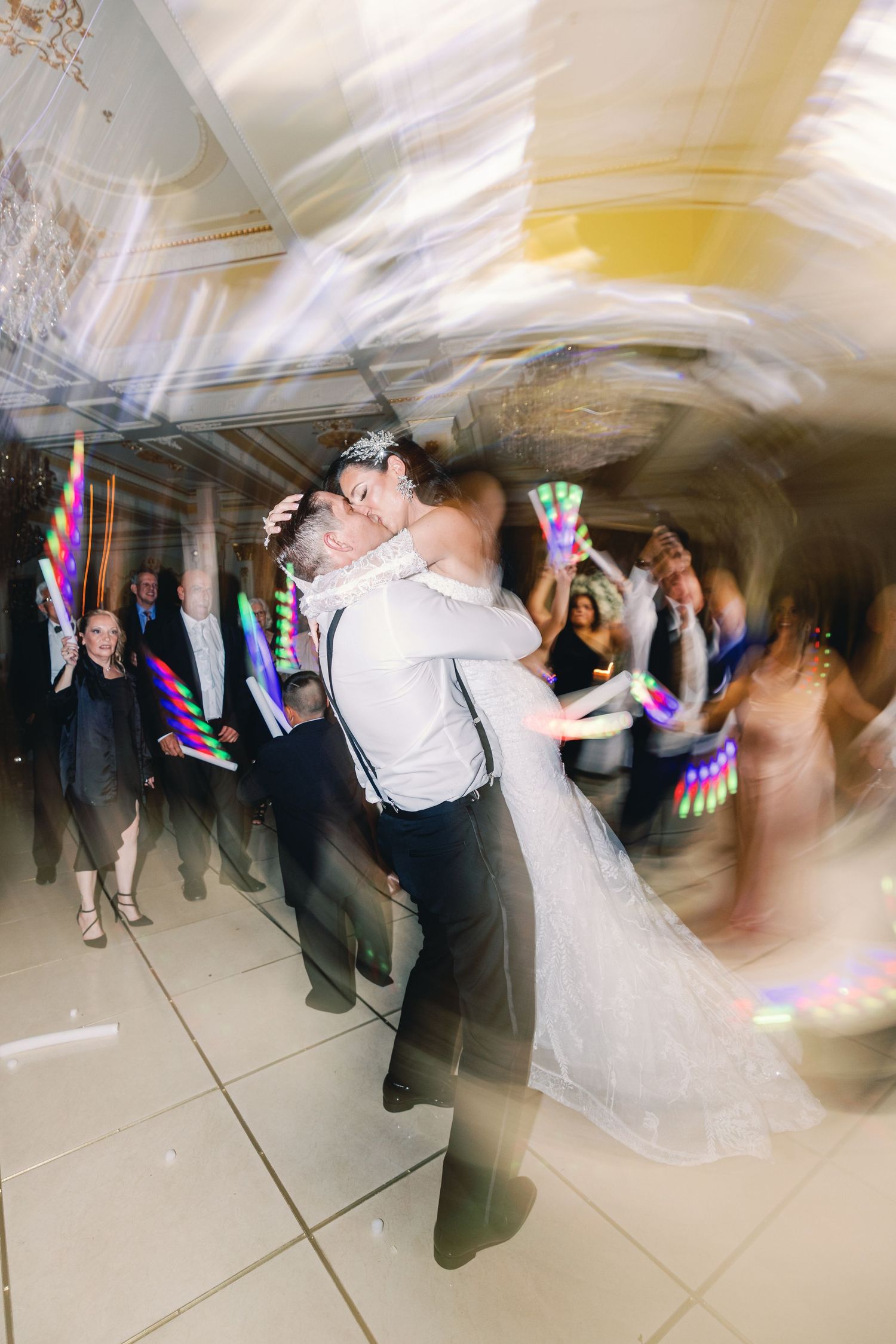 Bride and groom share first dance kiss surrounded by guests with glowing light sticks.