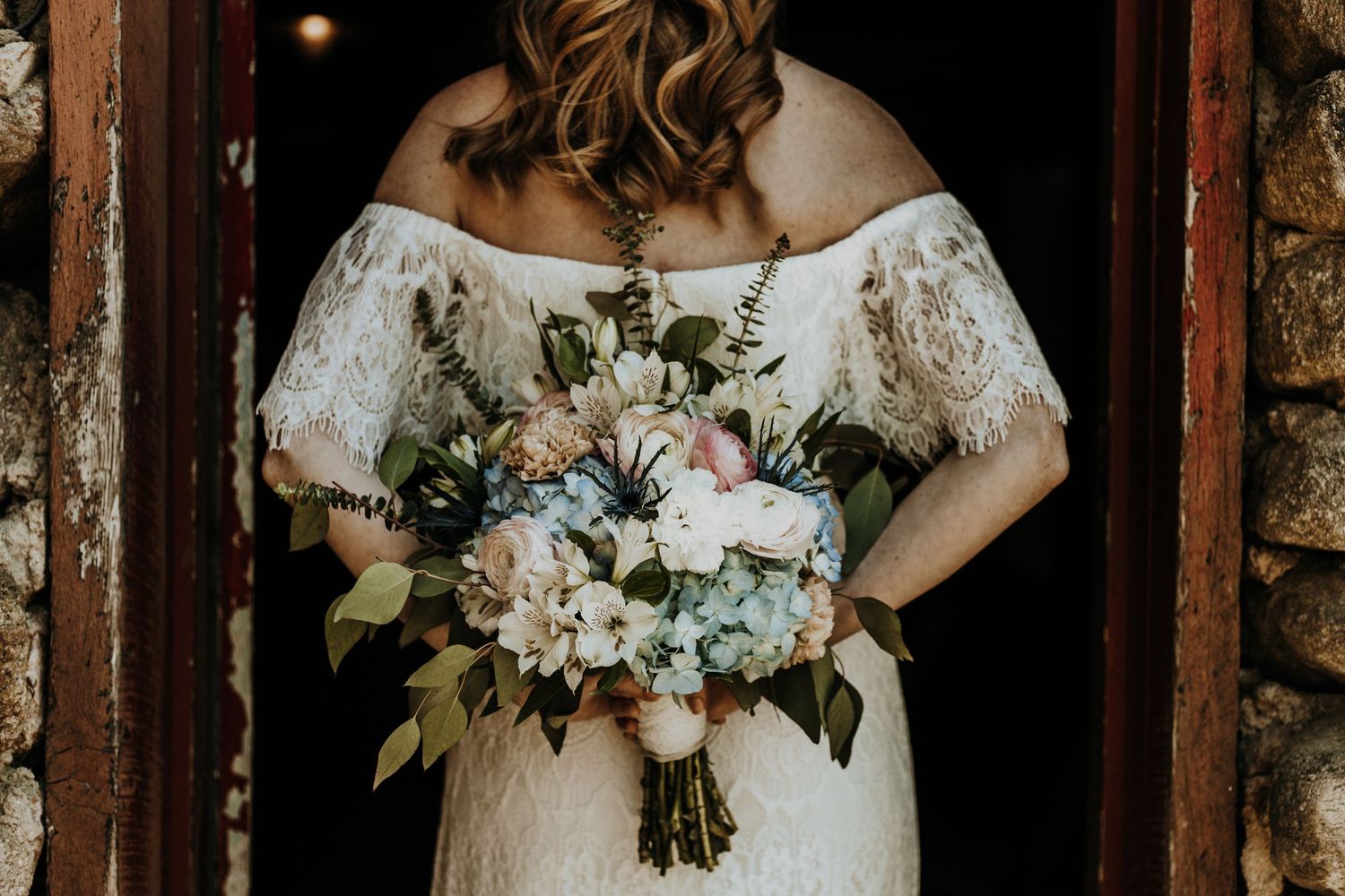 Back view of a bride in lace dress holding a bouquet of pastel flowers.