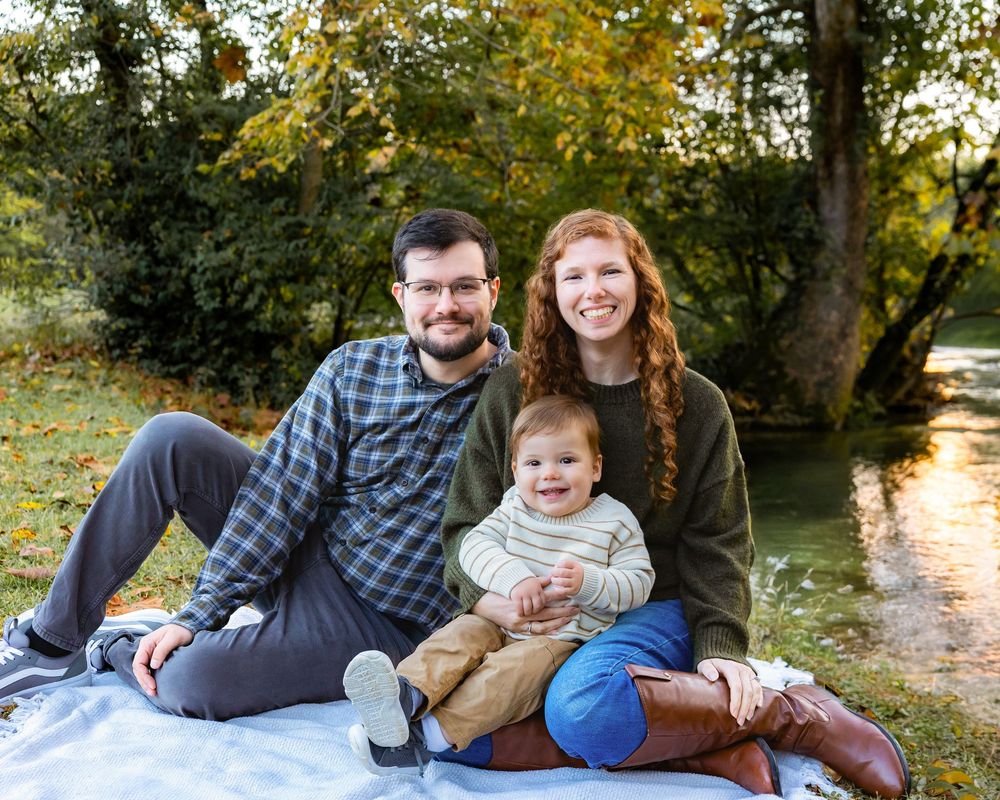 Family relaxing together on a blanket outdoors during a sunny autumn day in a park setting.