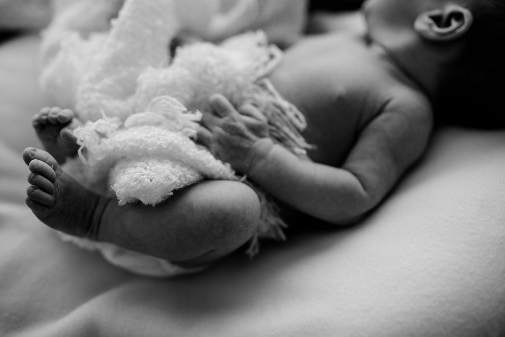 Black and white close-up of tiny newborn baby feet wrapped in delicate lace against a soft blurred background.Newborn Fotografie Frankfurt