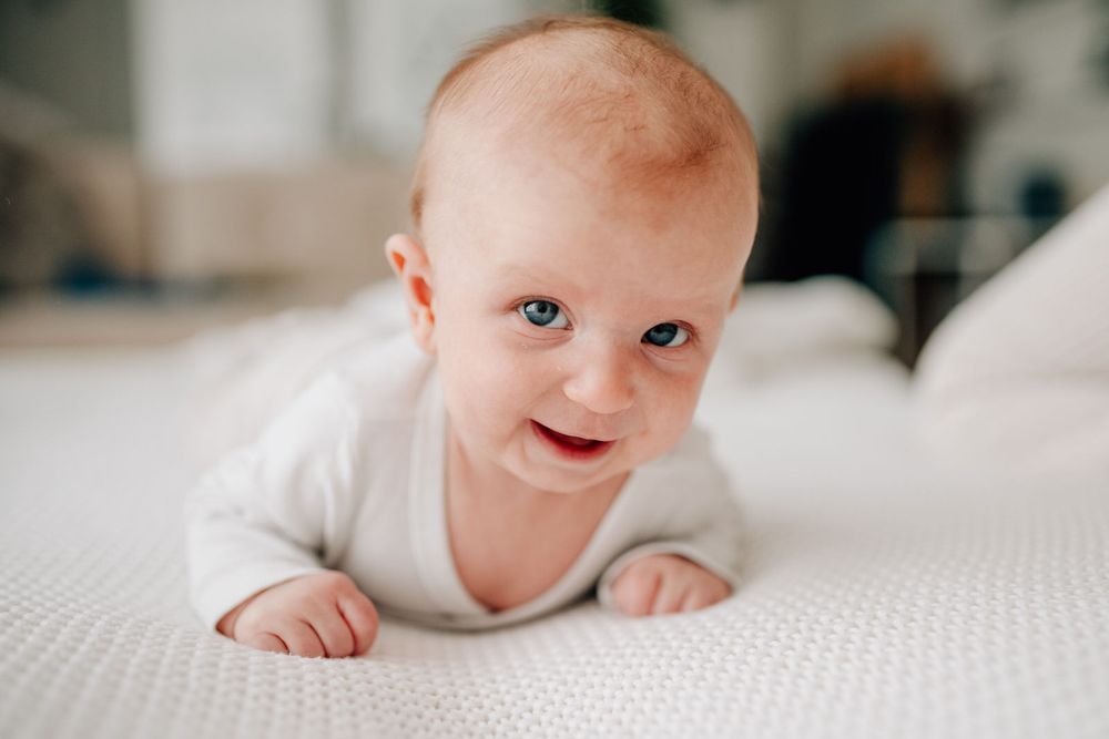 A smiling infant laying on their tummy on a white textured surface.
Newborn Fotografie Frankfurt