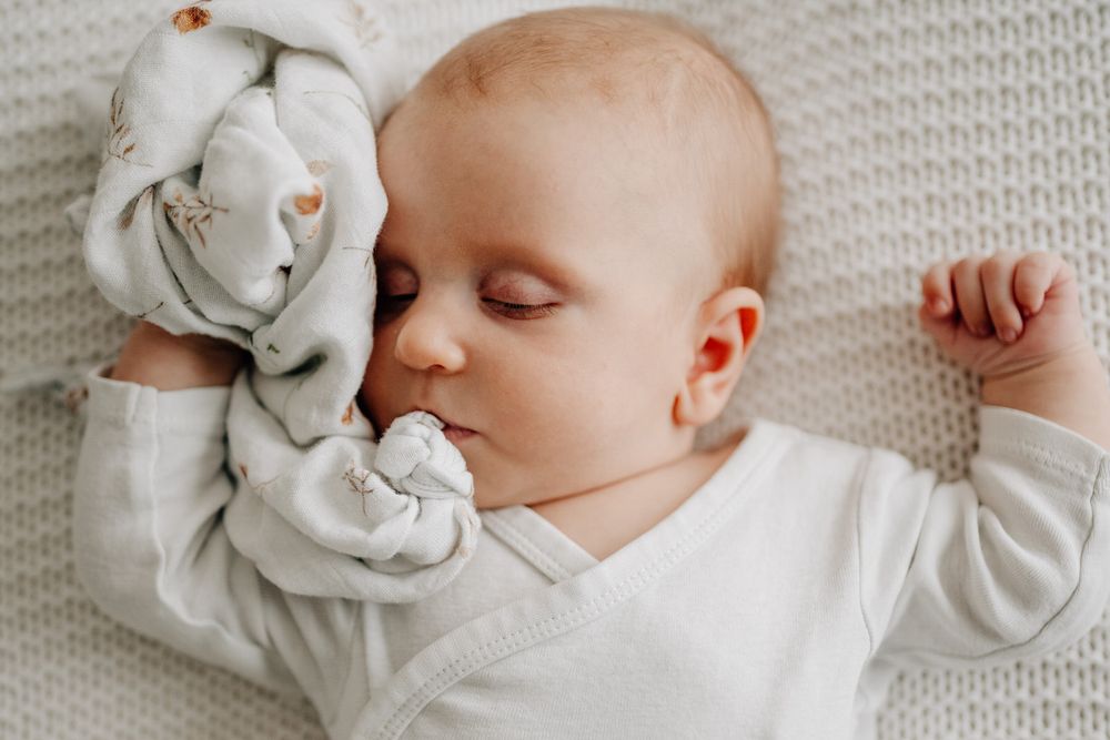 Sleeping baby in white clothing lies peacefully next to a plush stuffed animal on a textured blanket.Newborn Fotografie Frankfurt