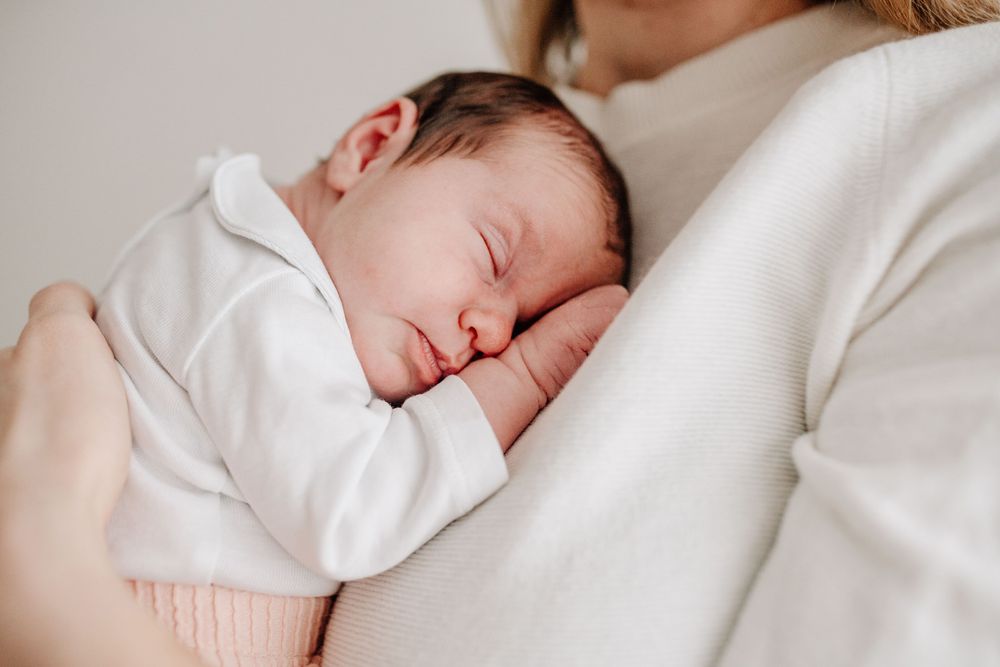 A peaceful newborn baby in white sleeps soundly against a soft cream-colored surface.Newborn Fotografie Frankfurt