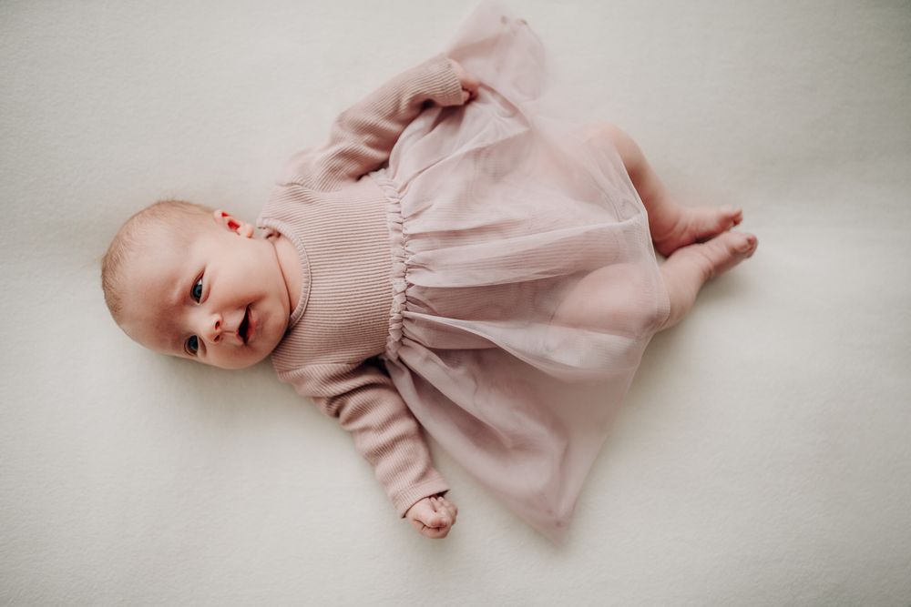 Sweet baby in a light pink dress lies on a neutral gray background looking sideways.Newborn Fotografie Frankfurt