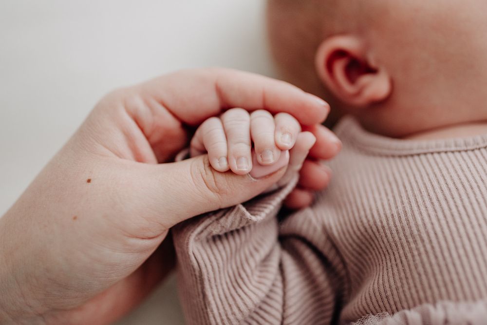 A tiny baby's hand grasps an adult's finger while wearing a soft pink knit sweater.Newborn Fotografie Frankfurt