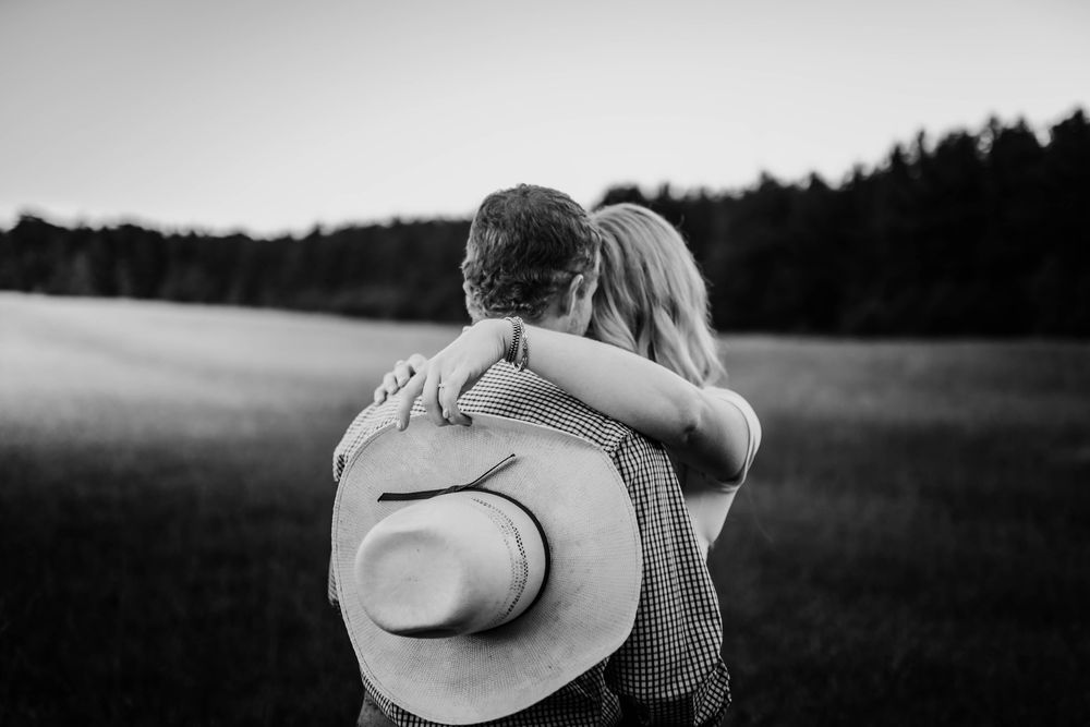 A romantic black and white photo showing an embrace in a field at dusk with a cowboy hat visible.