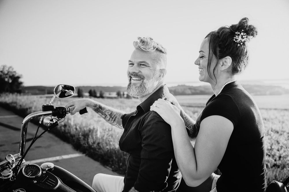 A couple shares a joyful moment together on a motorcycle against a scenic rural backdrop.