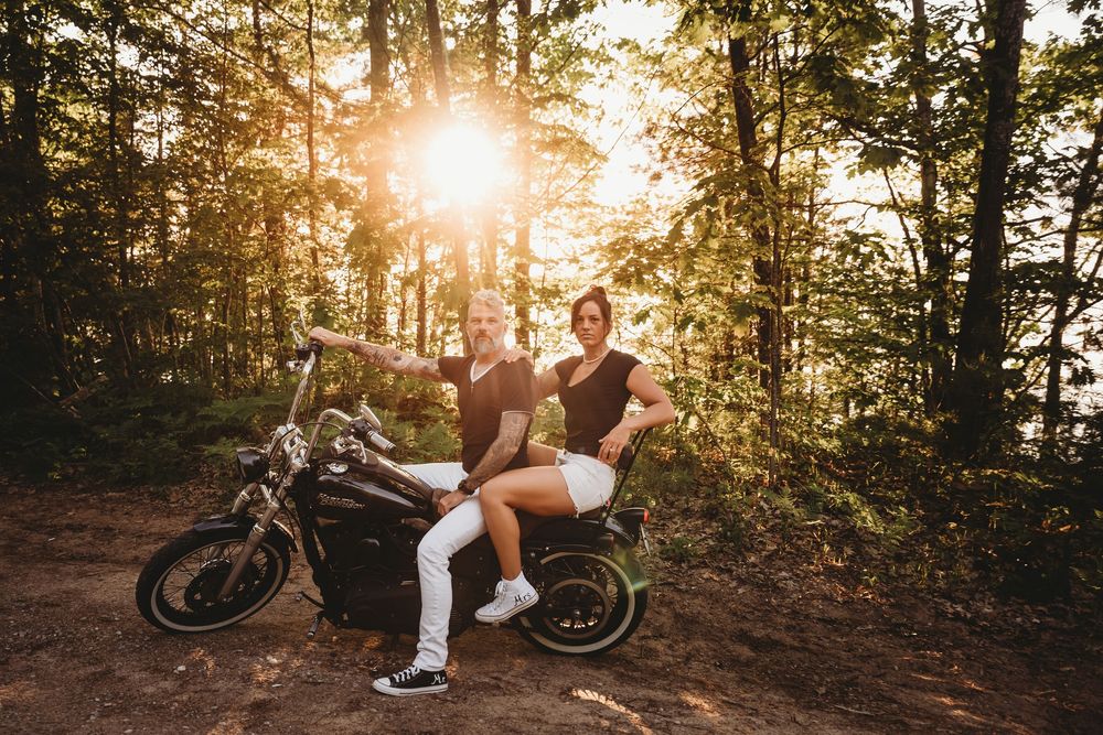 A motorcycle parked in a wooded area with sunlight streaming through the trees at golden hour.