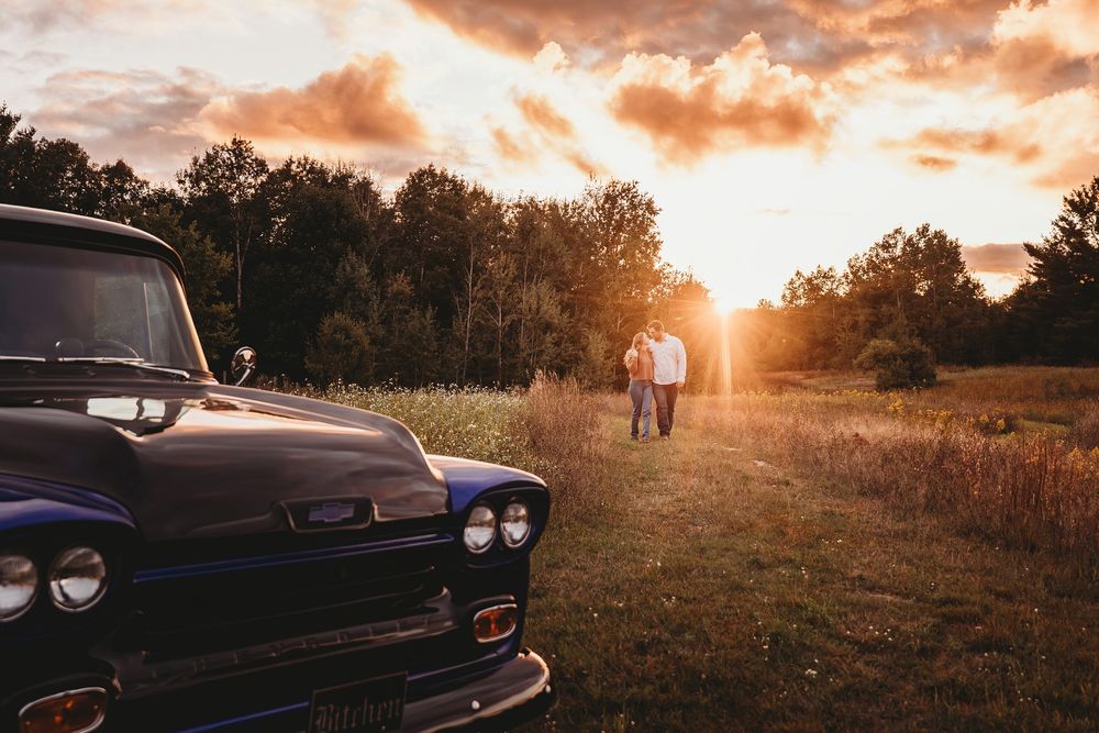 Classic car silhouetted against dramatic orange sunset sky with trees in background during golden hour.