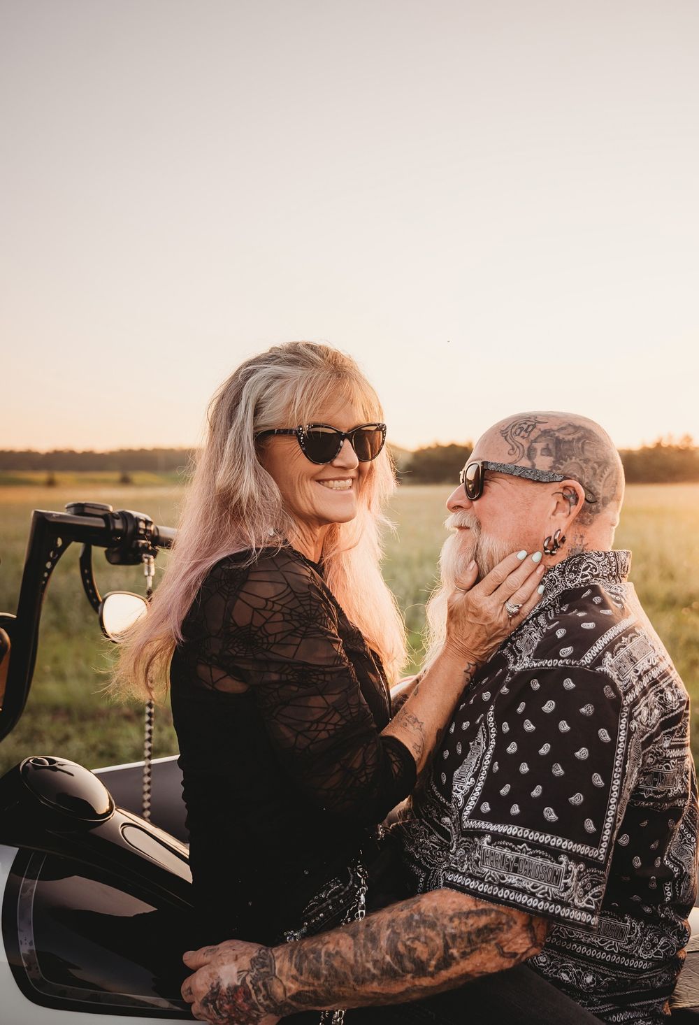 A tender moment shared between two people on a motorcycle at sunset in a field.