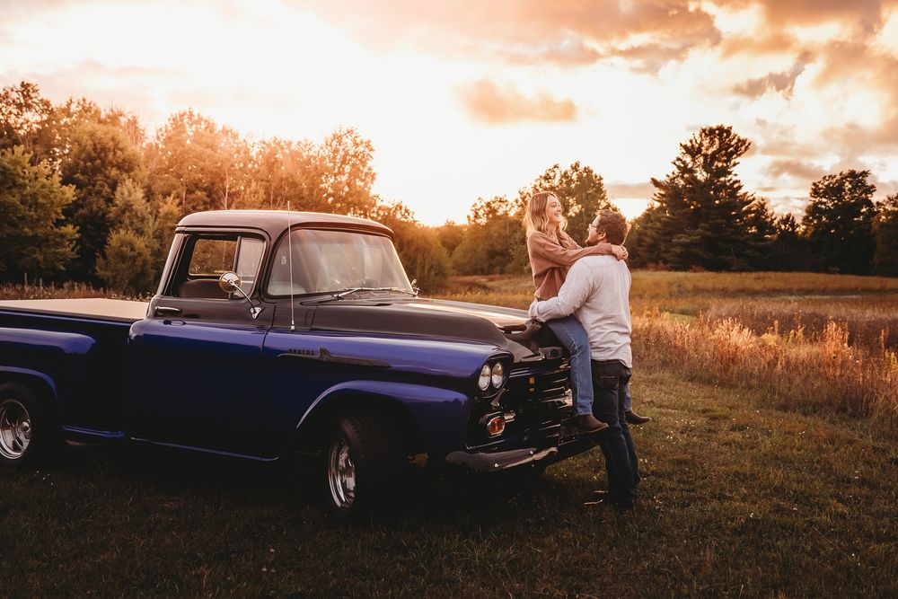 A classic blue vintage pickup truck parked in a golden field during sunset.