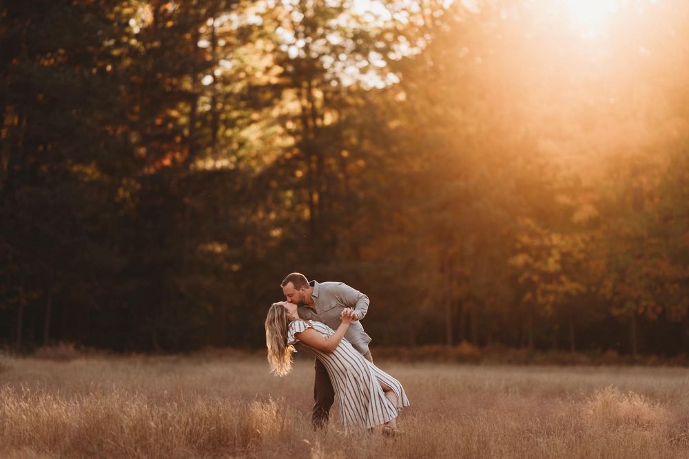 Silhouetted figures embrace in a golden sunset field with tall grass and trees in the background.