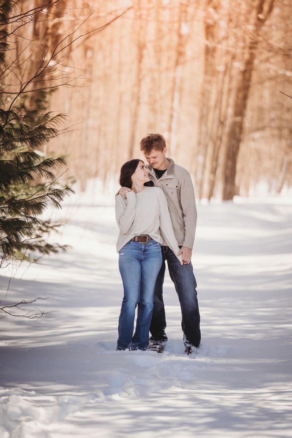 A romantic winter photoshoot in a snowy forest with pine trees creating a dreamy backdrop.