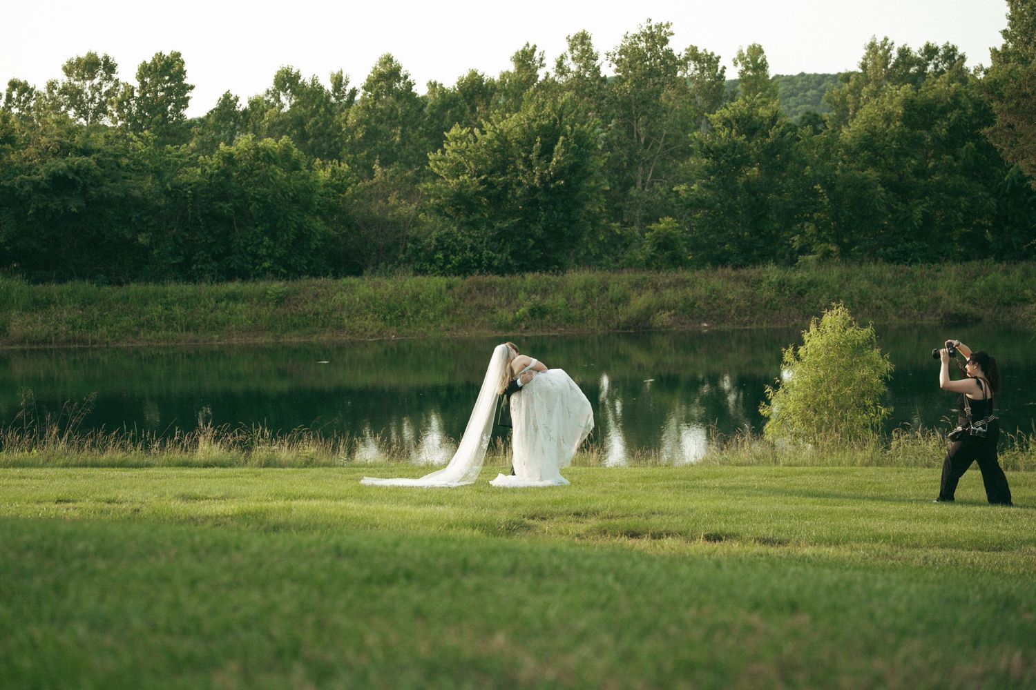 Wedding photographer capturing couple sitting on rustic bench in garden setting.
