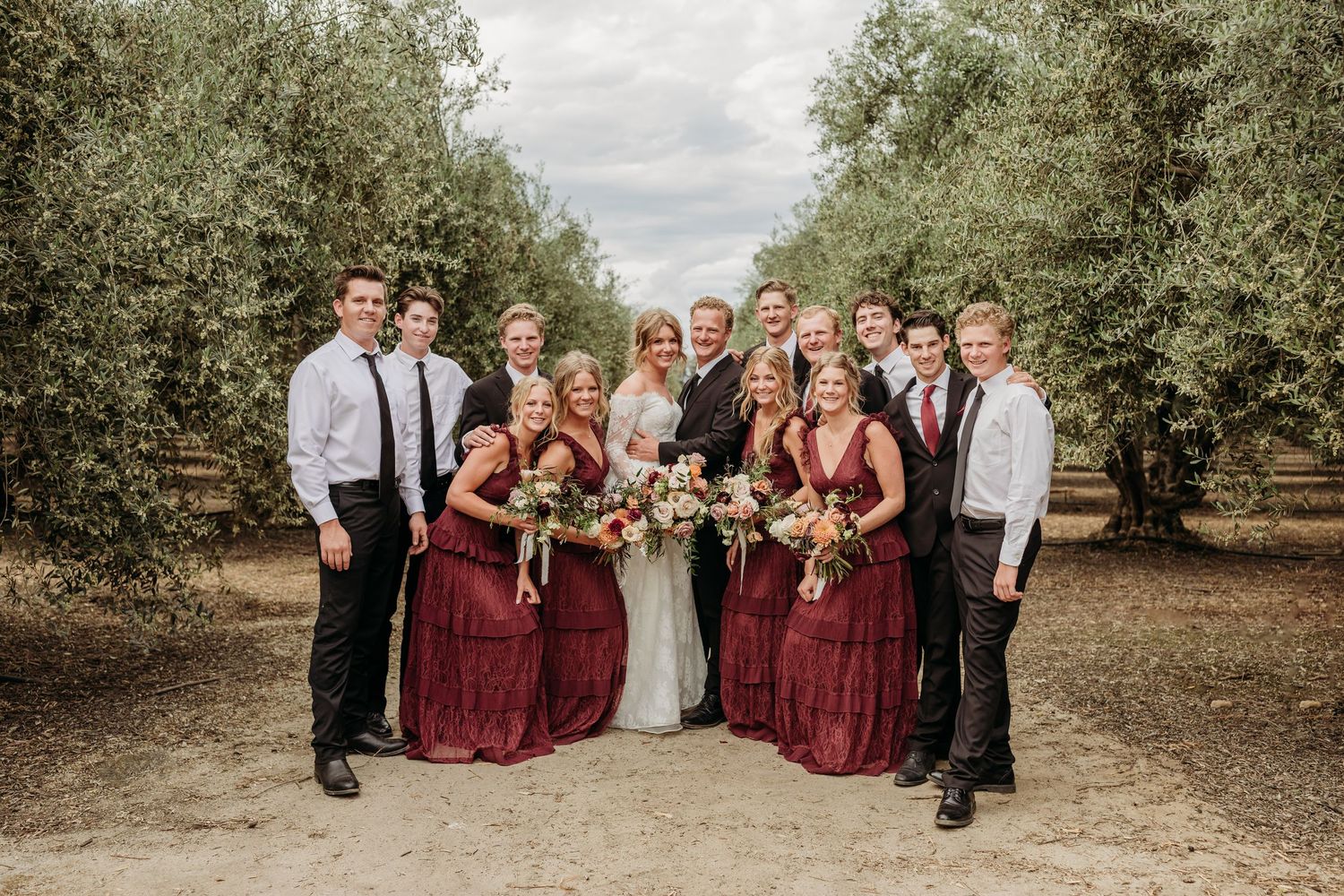 A wedding party poses together outdoors wearing black and white formal attire in a grassy field.