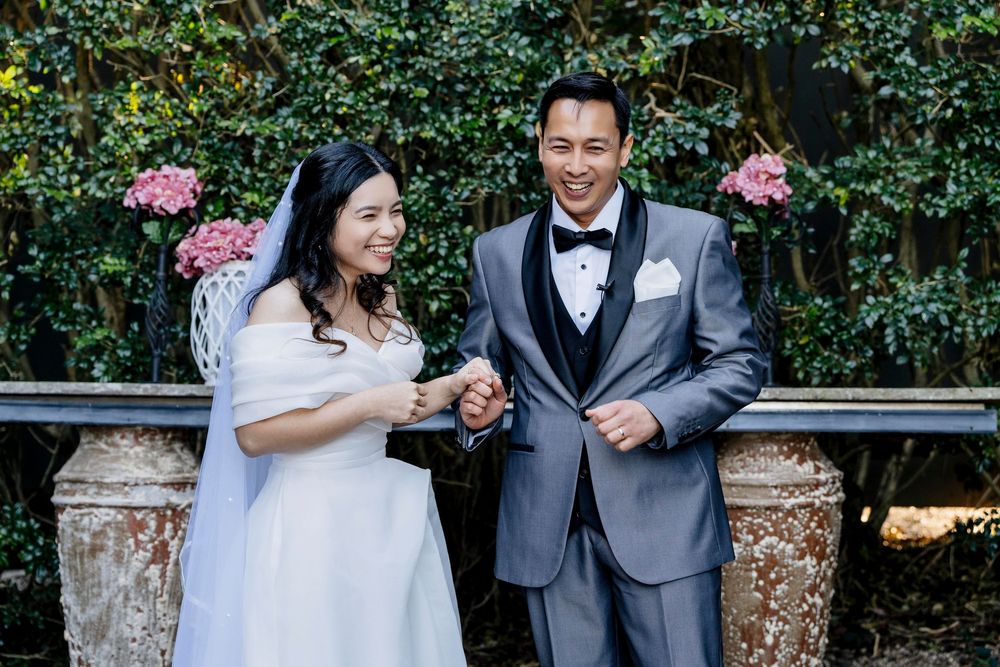 Romantic outdoor wedding celebration with couple toasting champagne glasses surrounded by lush greenery and flowers.