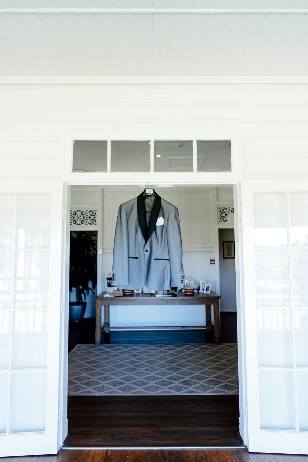 Interior view of an elegant white room with a blue-gray suit displayed on a mannequin and geometric patterned carpet.