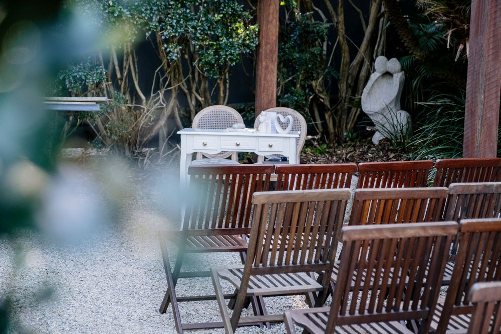 Rustic wooden benches line a peaceful outdoor garden patio area surrounded by lush greenery and trees.