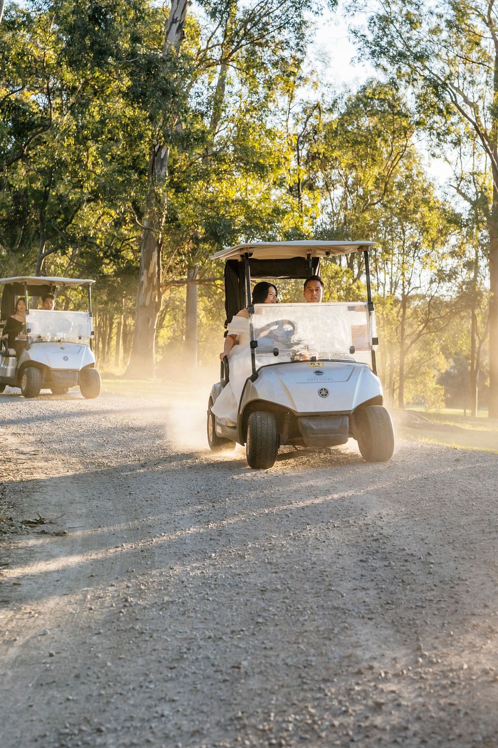 Golf carts driving down a dusty path through trees during golden hour creating a dreamy atmosphere.