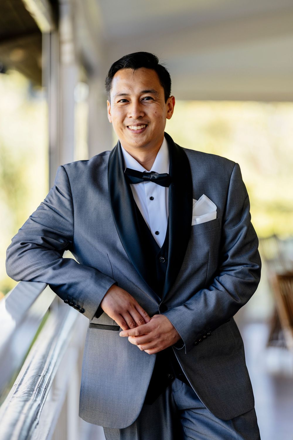 A person in a formal gray tuxedo and bow tie poses against a light background in a series of professional photos.