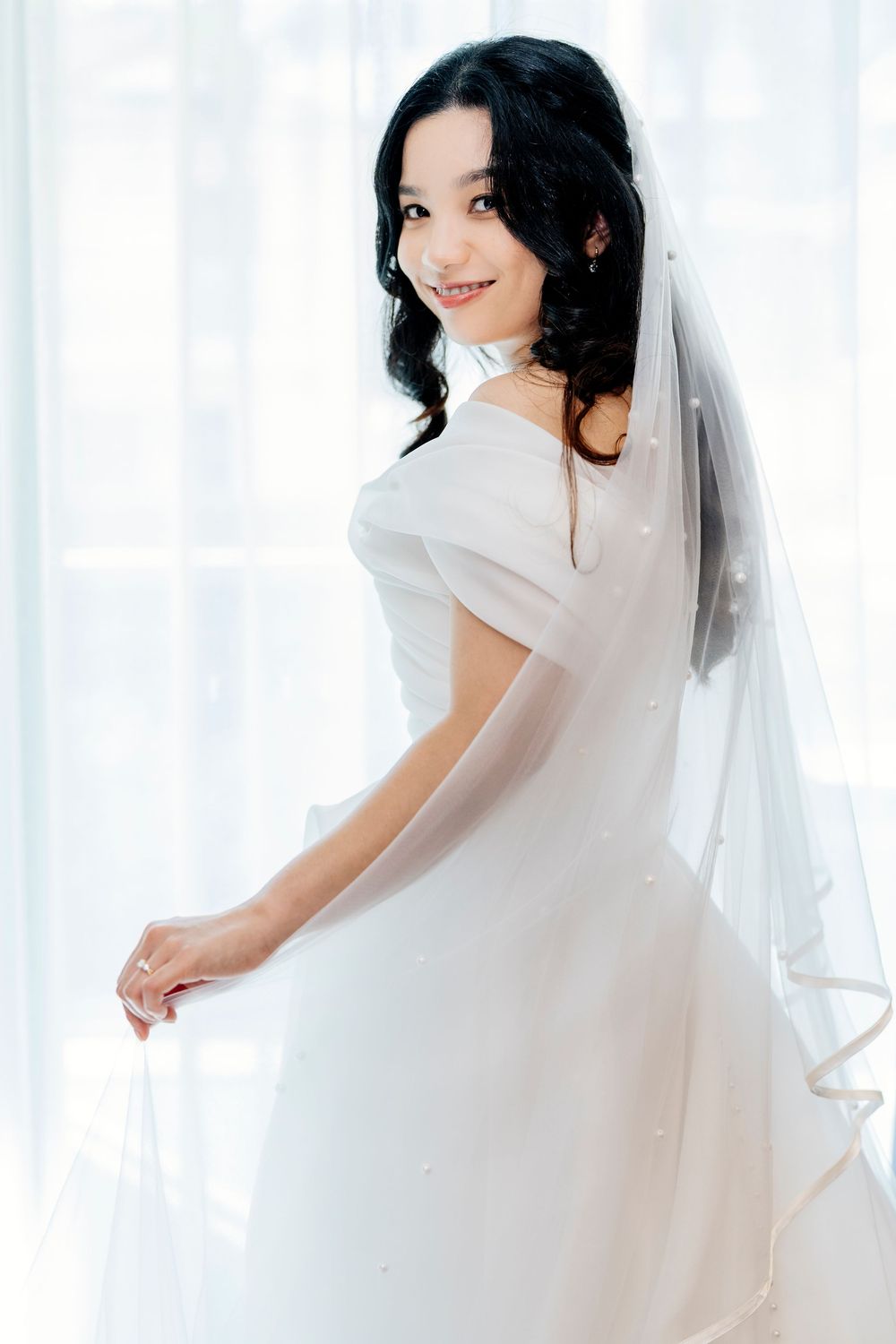 A bride in a flowing white wedding dress and veil poses gracefully against a light backdrop in a series of photos.