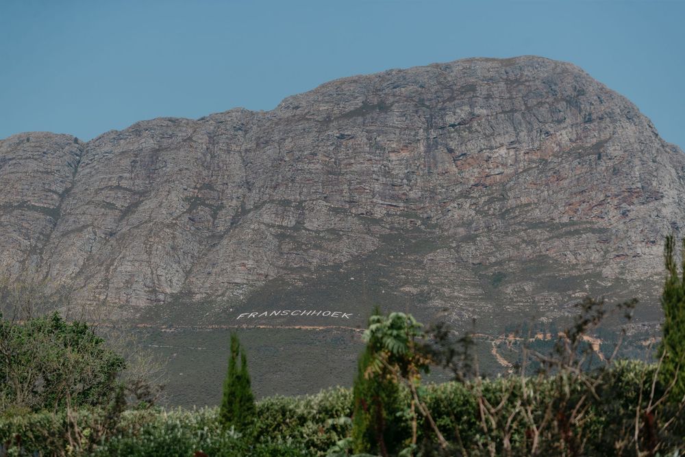 Panoramic view of rugged mountain peaks and cliffs against a blue sky with sparse vegetation in the foreground.