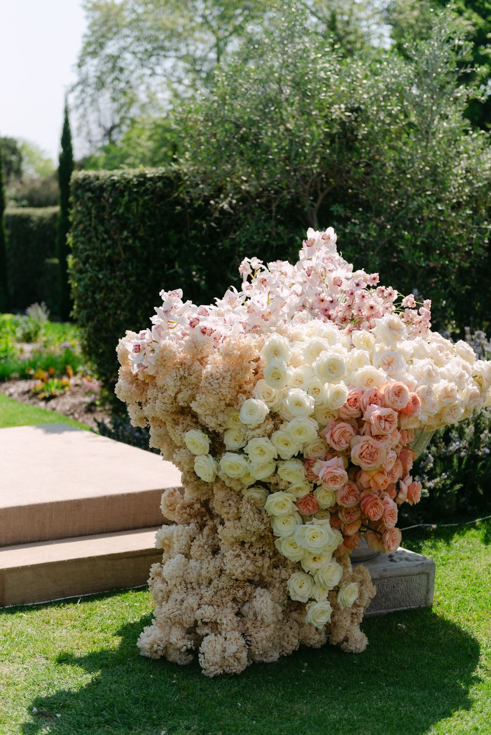A stunning display of cascading white and blush pink flowers arranged on a wooden bench in a garden setting.