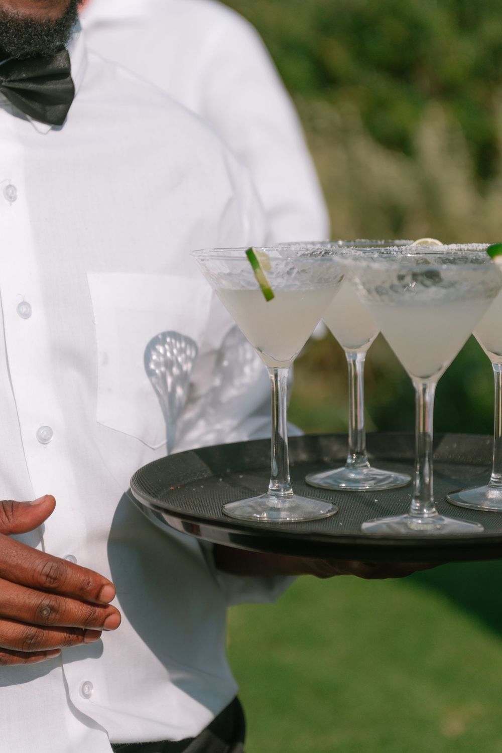 Server holding a tray with frosted martini glasses filled with clear cocktails and garnished with lime.