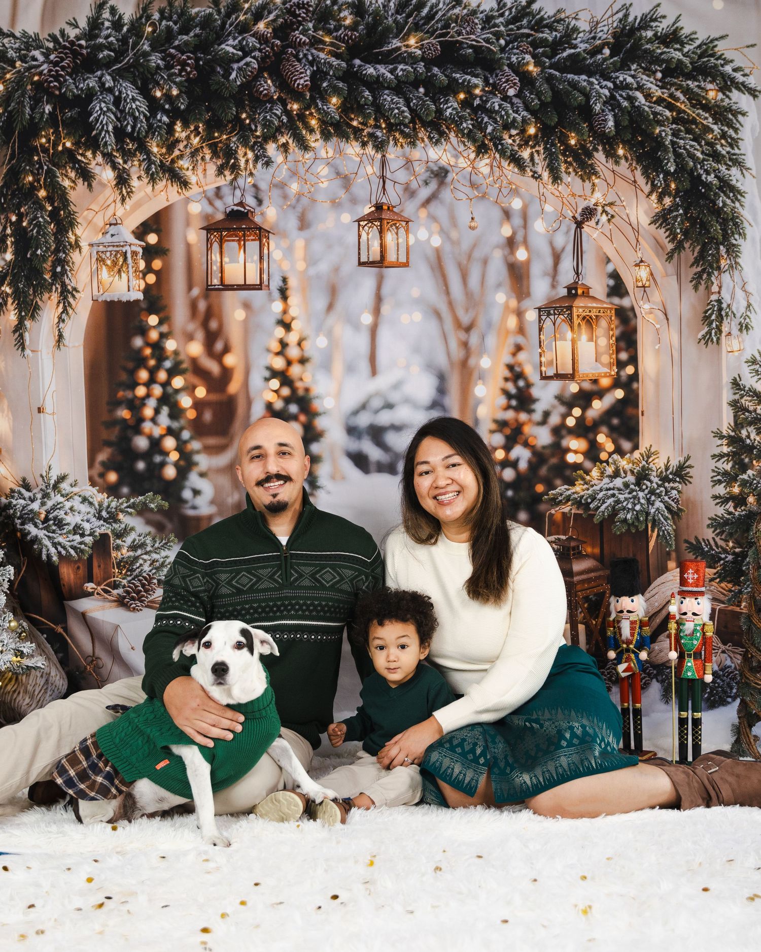Family with dog poses in cozy winter sweaters against festive holiday backdrop with lanterns.