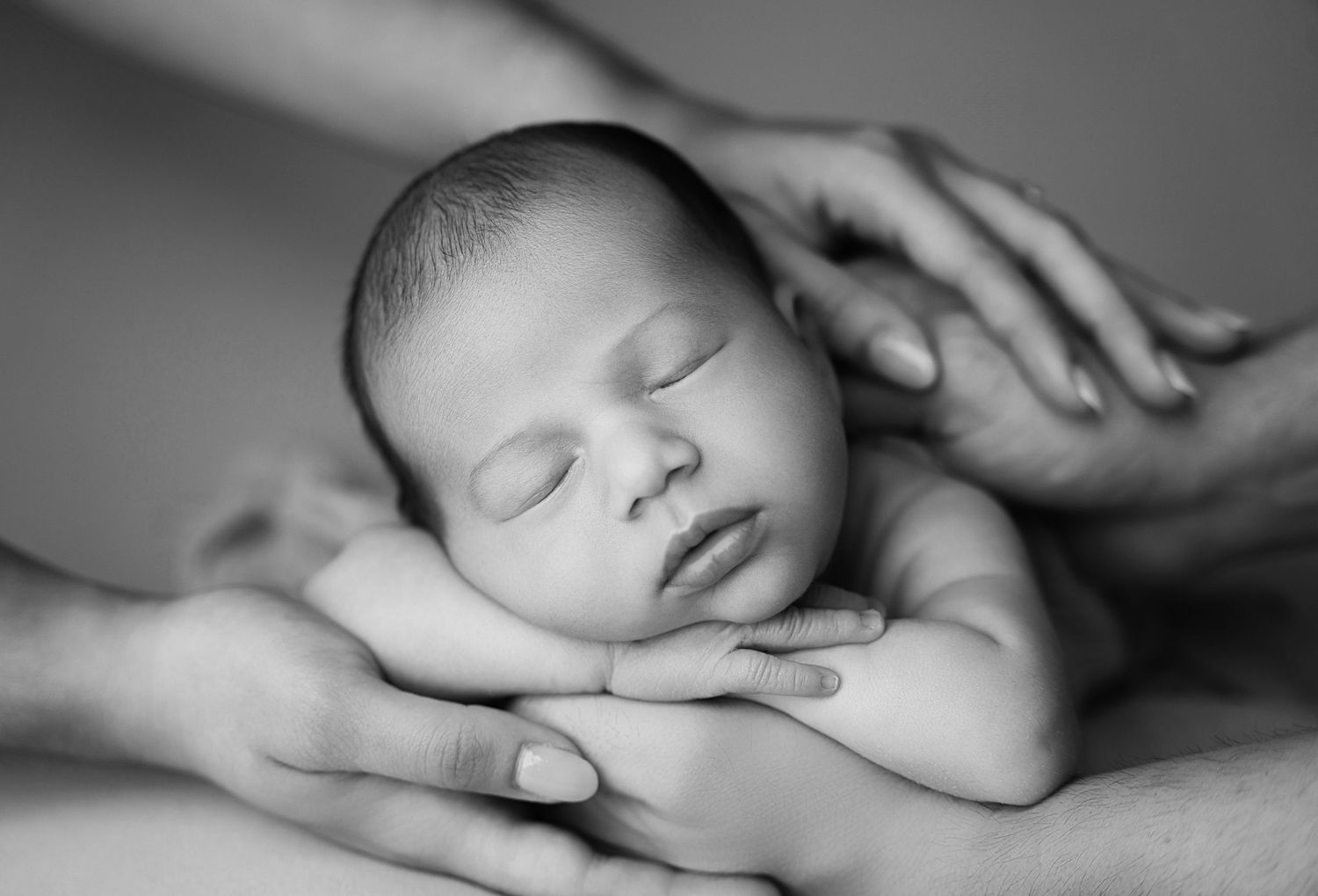 Miami Maternity photographer A peaceful sleeping newborn baby rests in gentle hands in a black and white portrait.