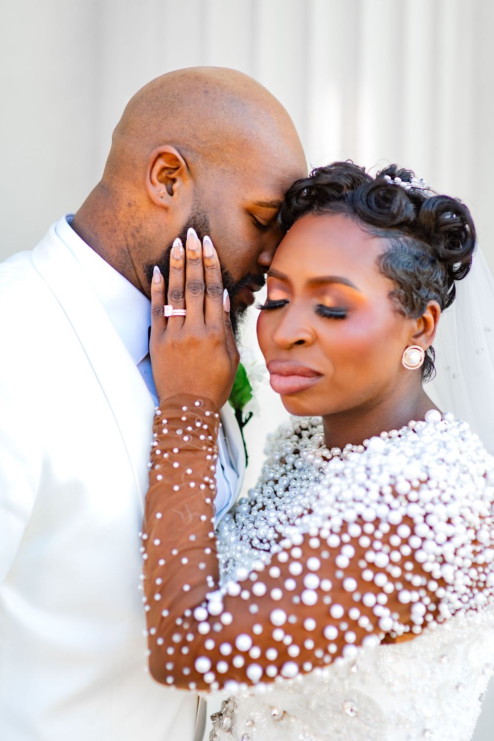 Romantic wedding couple in intimate poses wearing elegant white attire with pearl details.