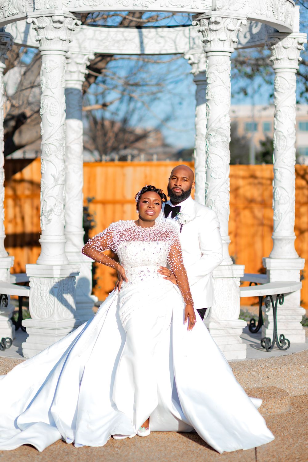 A wedding photoshoot featuring a flowing white ballgown against white columns and an orange fence background.