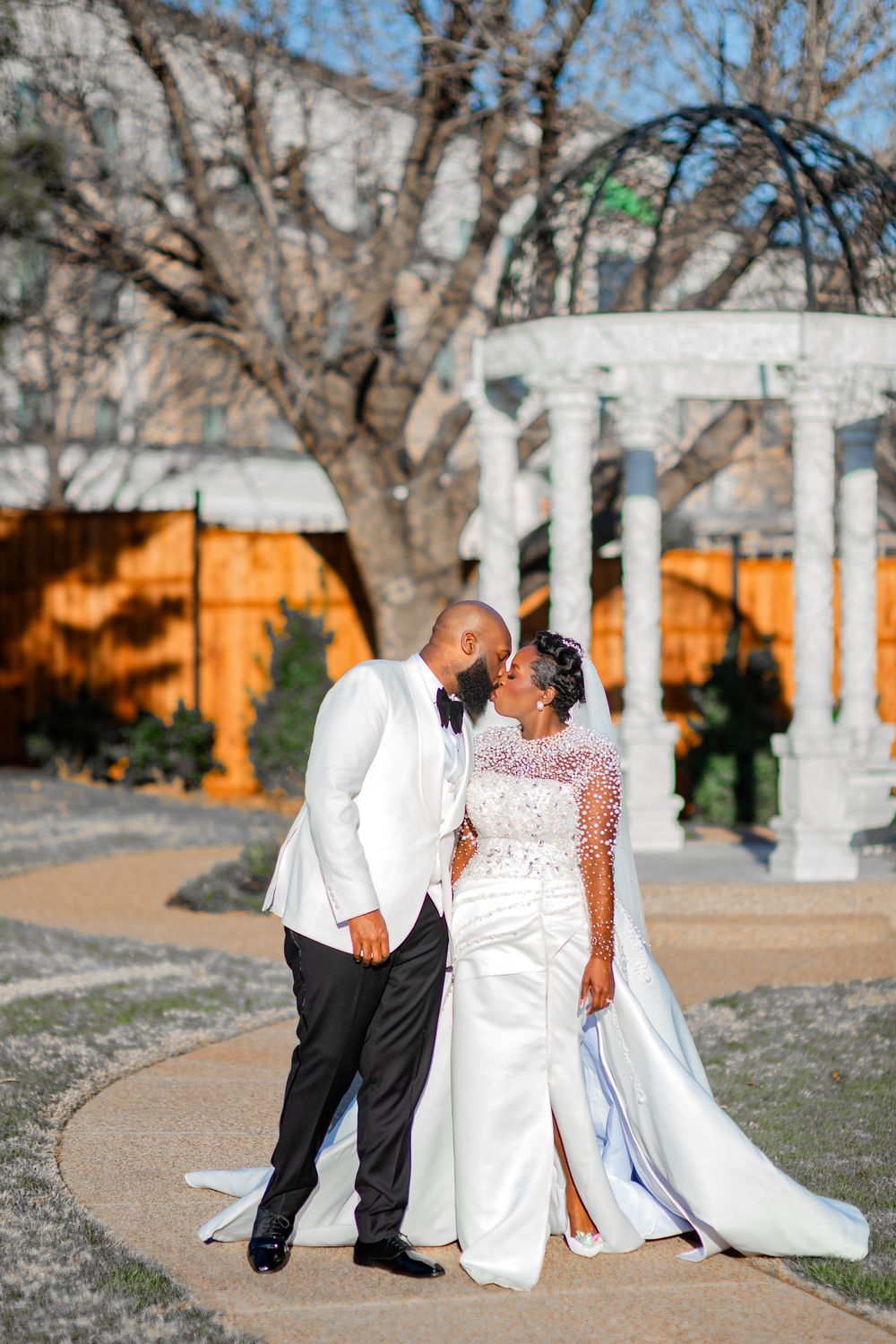 Wedding couple poses playfully in front of decorative white columns outdoors.