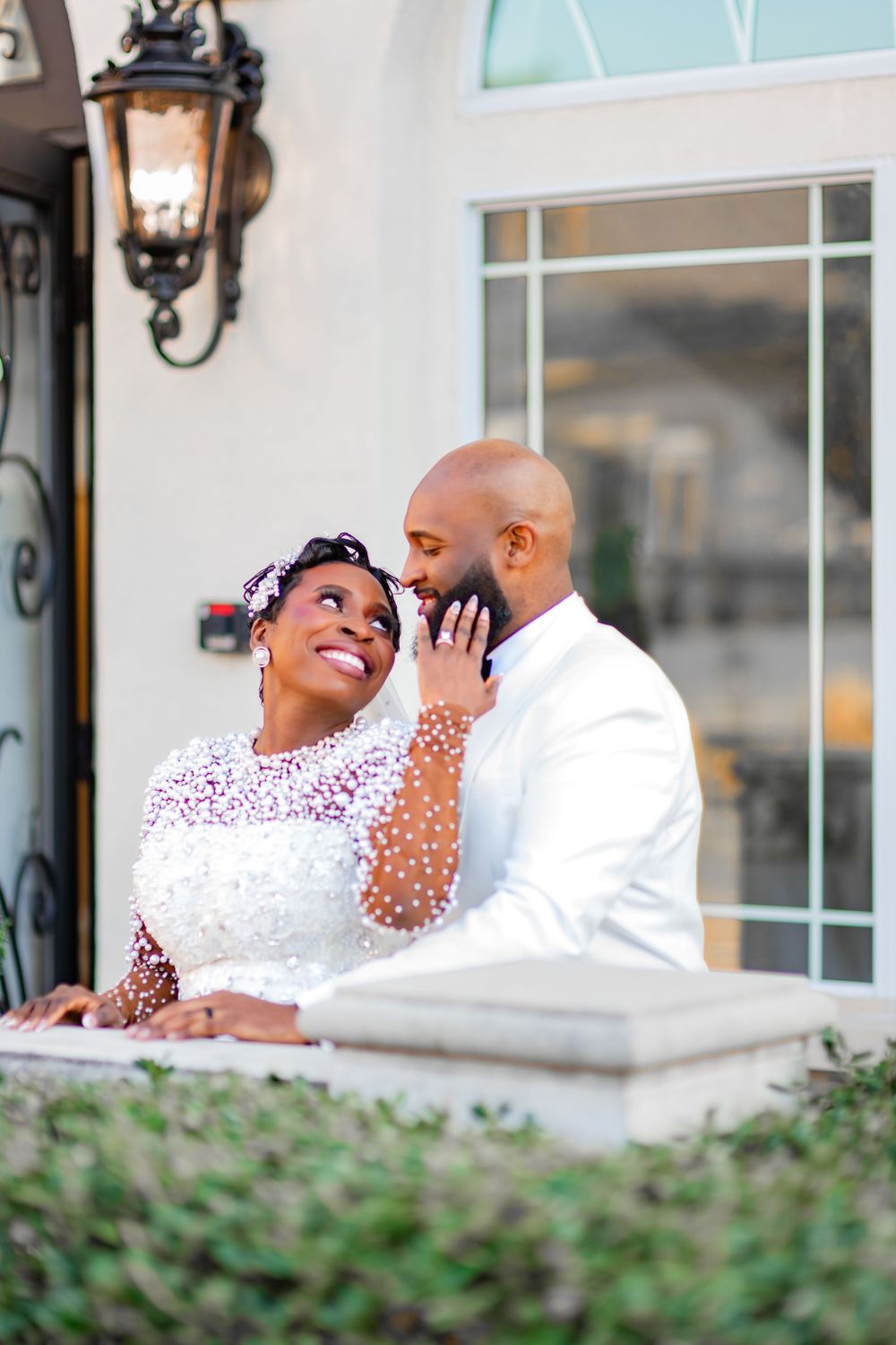 A loving couple shares a tender moment on a balcony with decorative lantern and greenery in the background.