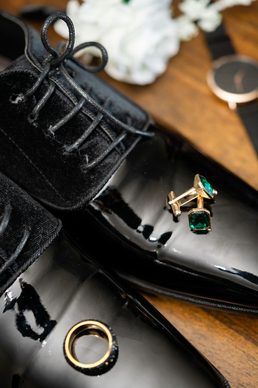 Polished black leather dress shoes with green gemstone cufflinks on wooden table.