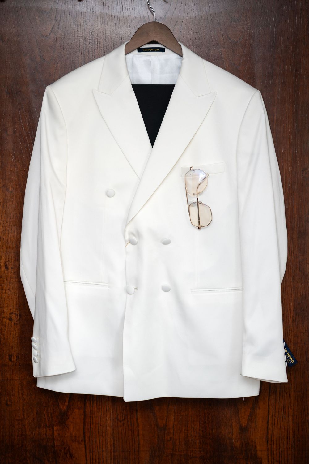 Row of crisp white suit jackets displayed on wooden hangers against a dark wood wall.