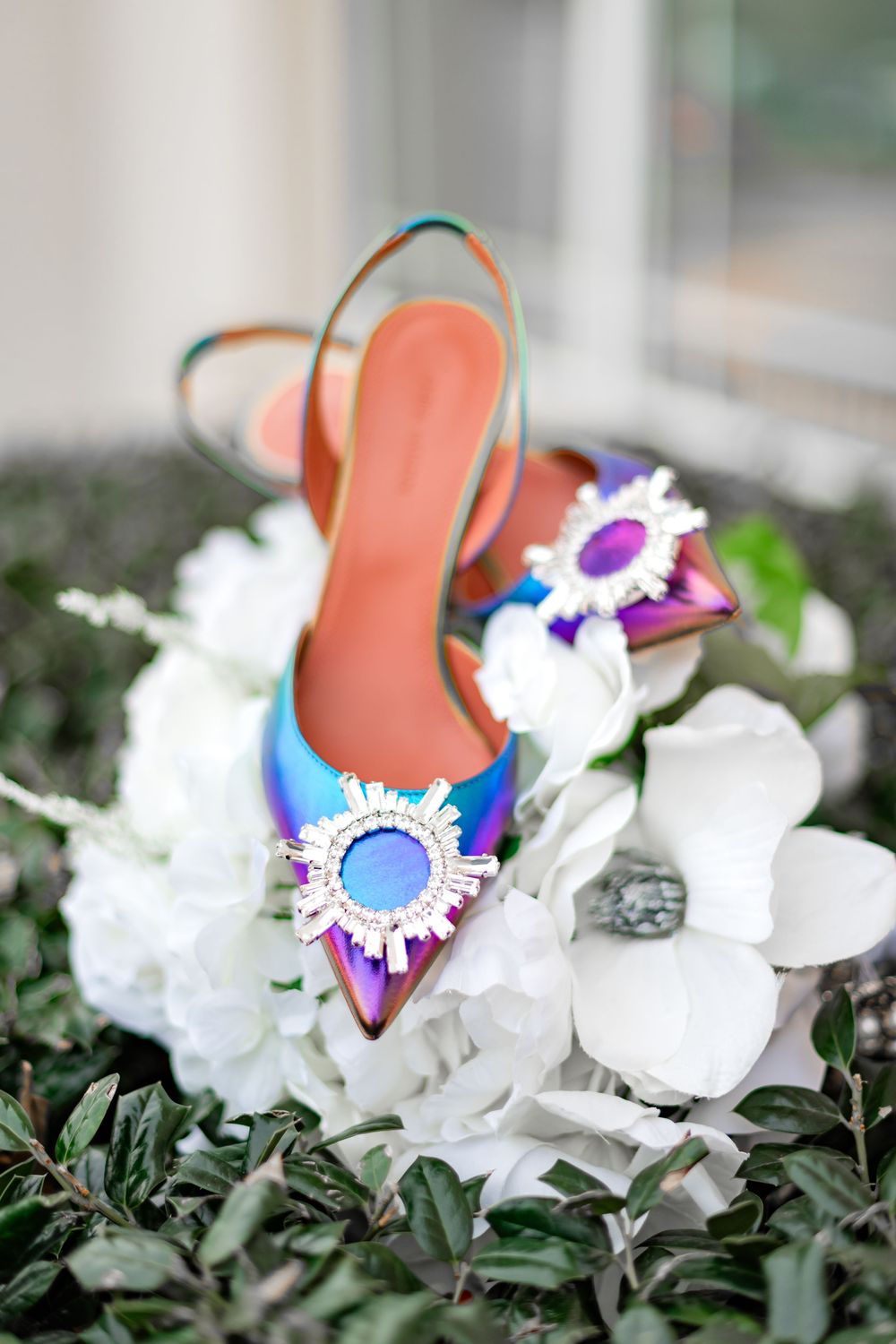 Orange flip flop sandal decorated with colorful flowers rests on a bed of white petals and green foliage.
