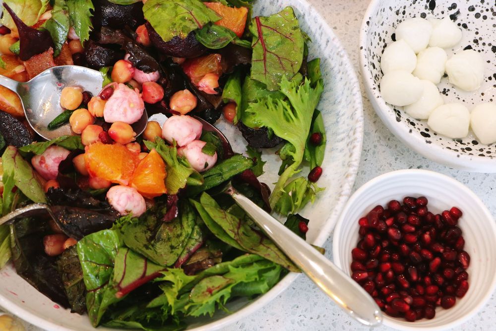Fresh salad with mixed greens, pomegranate seeds, and a side of creamy dressing on white plates.
