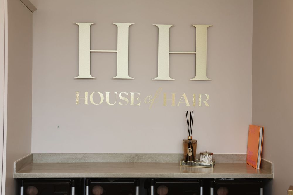 House of Hair salon reception desk featuring elegant HH logo signage on a cream wall.
