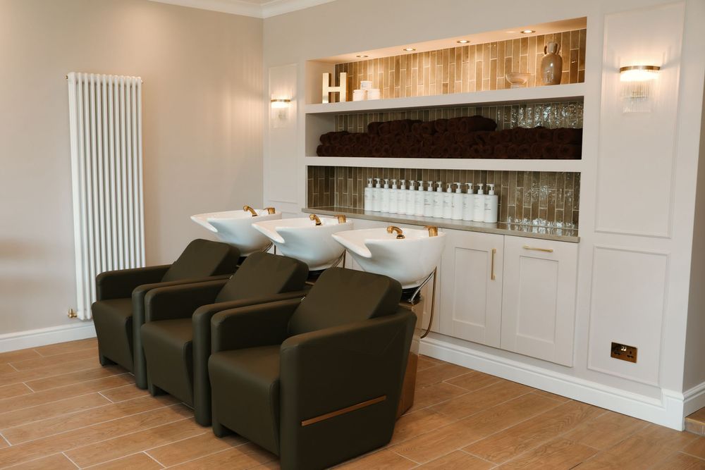 House of Hair salon wash area with brown chairs, white basins, and product shelving with wooden backdrop.