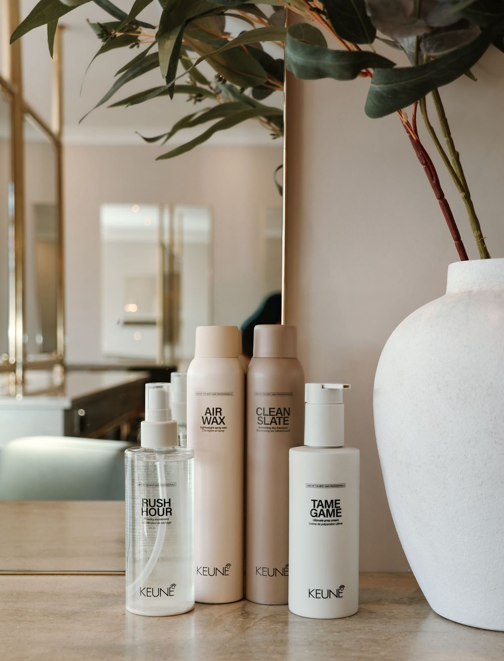 Keune hair care products including Rush Hour, Air Wax, Clean Slate, and Tame Game arranged on a marble surface.