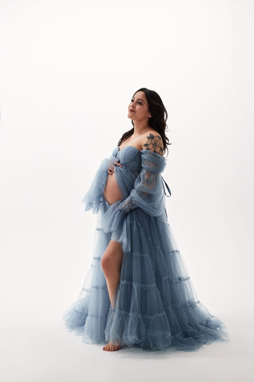 Ethereal maternity portrait featuring a flowing light blue tulle gown against a white backdrop.