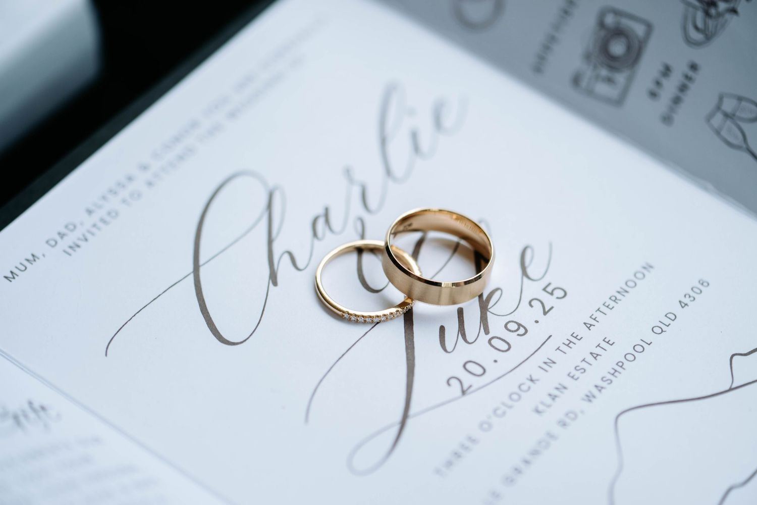 Two gold wedding rings rest on white paper with elegant cursive handwriting visible in the background.